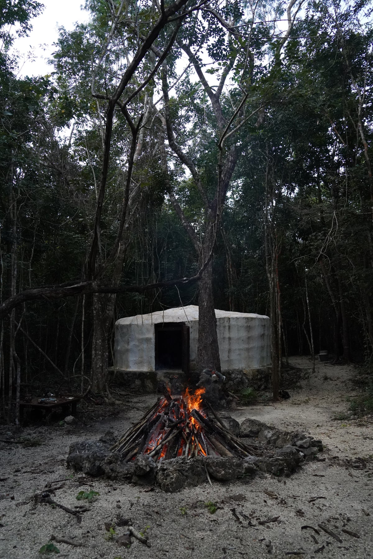 Fuego encendido frente al temazcal, entre los árboles.